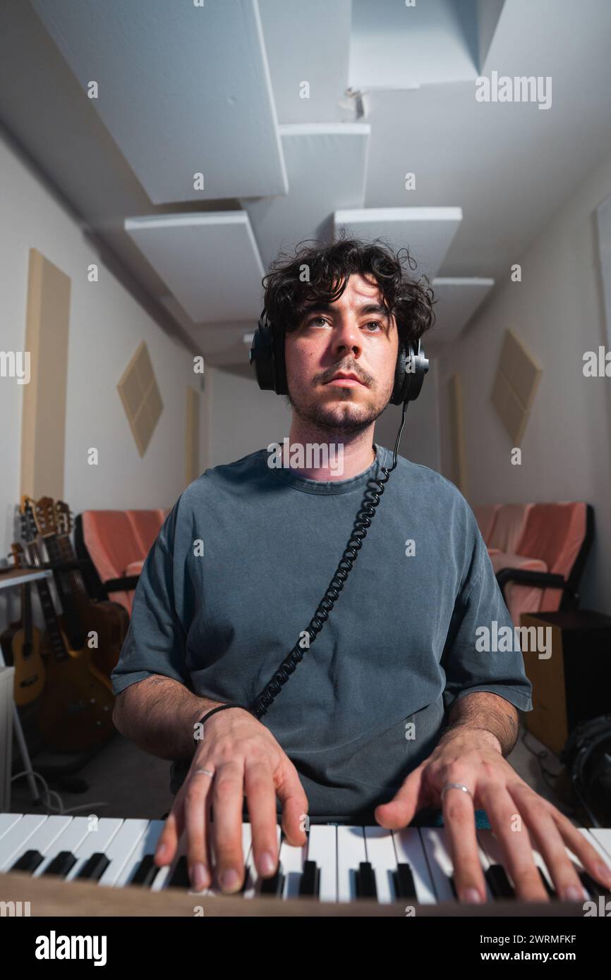 Ein fokussierter Mann spielt eine Tastatur in einem schalldichten Aufnahmestudio, während er Kopfhörer trägt. Stockfoto