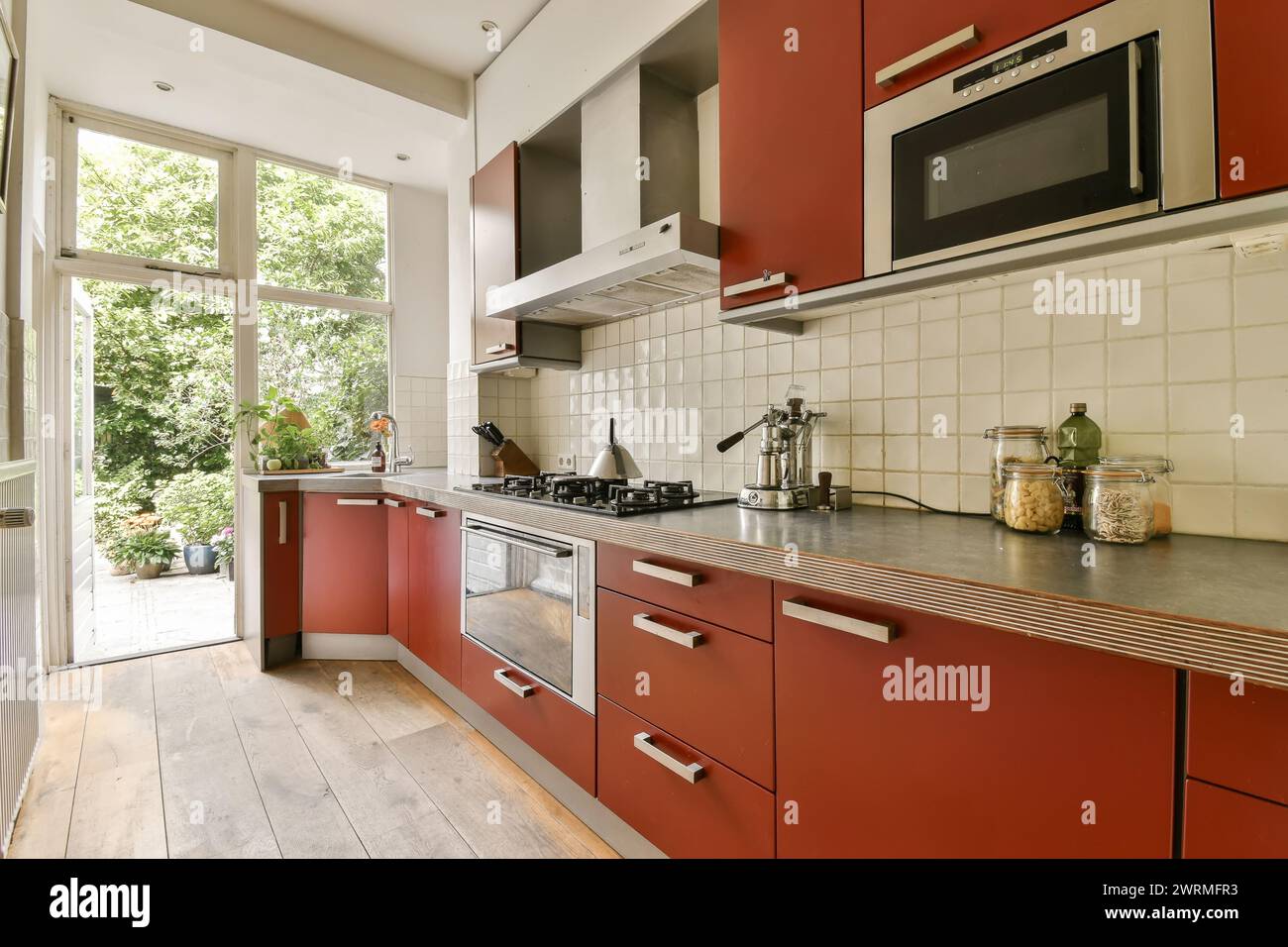 Die moderne Küche verfügt über elegante rote Schränke, Edelstahlgeräte und ein großes Fenster mit viel Tageslicht. Stockfoto