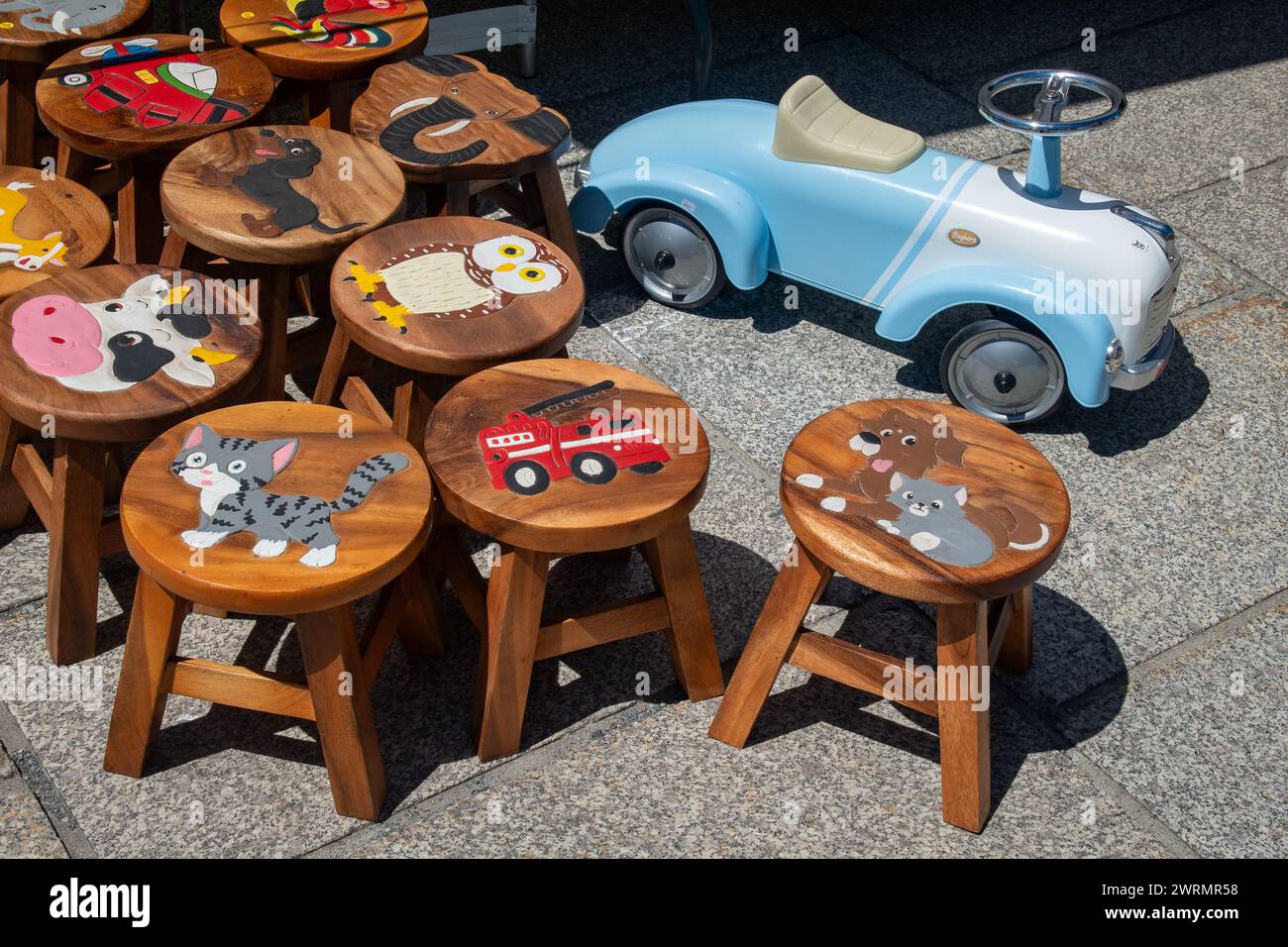 Handbemalte Holzhocker für Kinder und ein altes Tretspielzeugauto auf dem Wochenmarkt des beliebten Skigebiets Chamonix, Haute Savoie, Frankreich Stockfoto