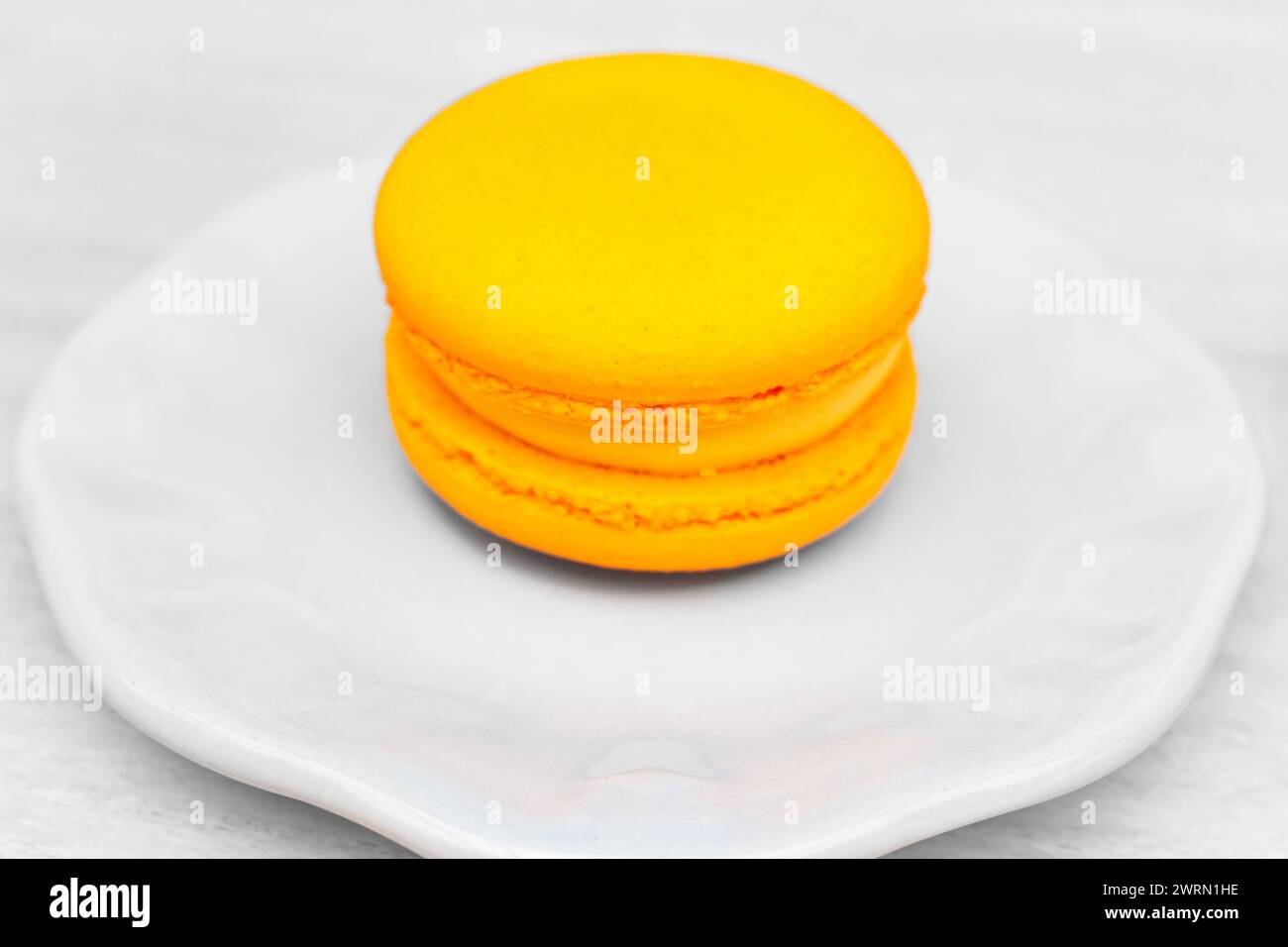 Makronen auf weißem Teller im Café. Macaron-Kuchen mit Orangenfruchtcreme. Süßes Food-Konzept. Nachtisch am Morgen. Orangenmakaron, isoliert. Stockfoto