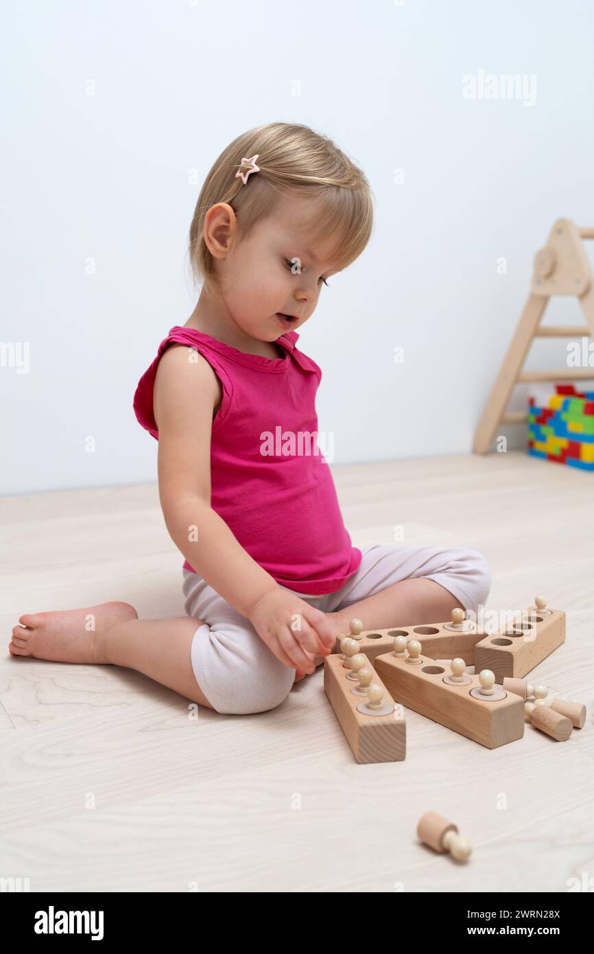 Ein 2,5-jähriges Kind sortiert Formen unterschiedlicher Größe. Holz-Kinderspiel nach Montessori-System. Hölzerne Noppzylinder für Vorschulspiele Stockfoto