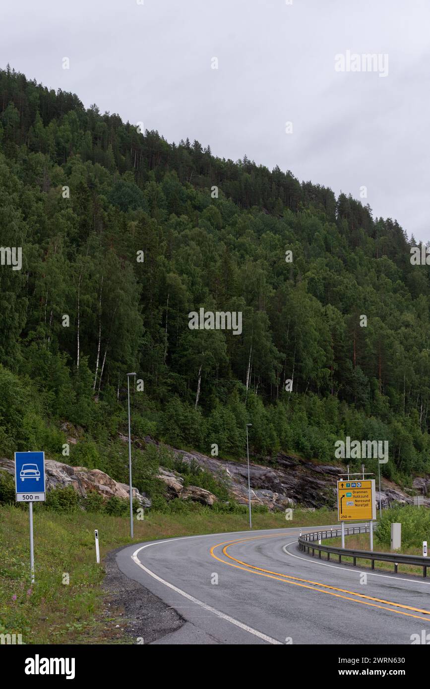 highway mit einer scharfen Kurve nach rechts am Fuße der Berge, die an einem nebeligen Tag mit grünen Bäumen bedeckt sind. Stockfoto