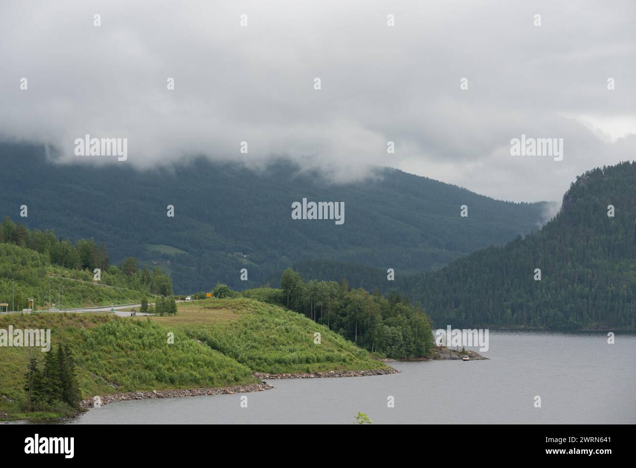 fluss in Norwegen fließt an einem nebeligen Tag entlang von Bergen mit grünen Bäumen und neben einer Autobahn. Stockfoto