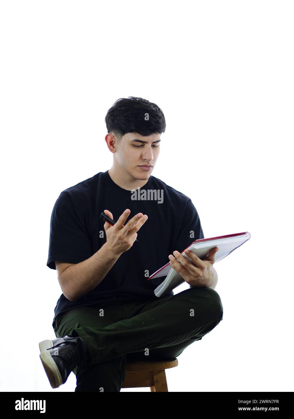 Vertikales Bild eines konzentrierten jungen Mannes, der Berechnungen macht, mit weißem Hintergrund sitzt und ein Notizbuch hält, mit Platz für Text Stockfoto