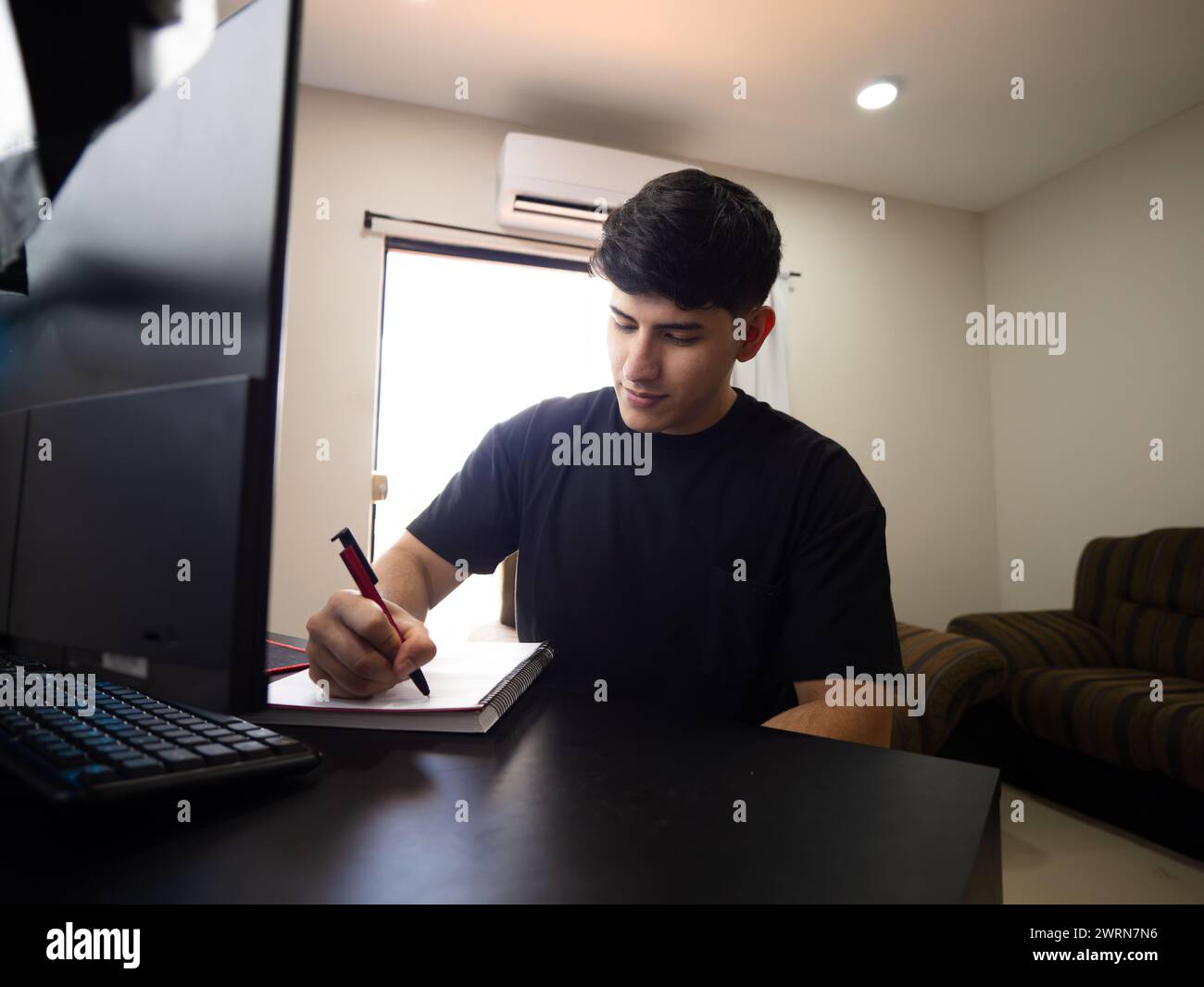 Bild eines Studenten, der Hausaufgaben zu Hause macht, vor seinem Computer sitzt. Fernunterricht, akademische Arbeit und Online-Lernen Stockfoto