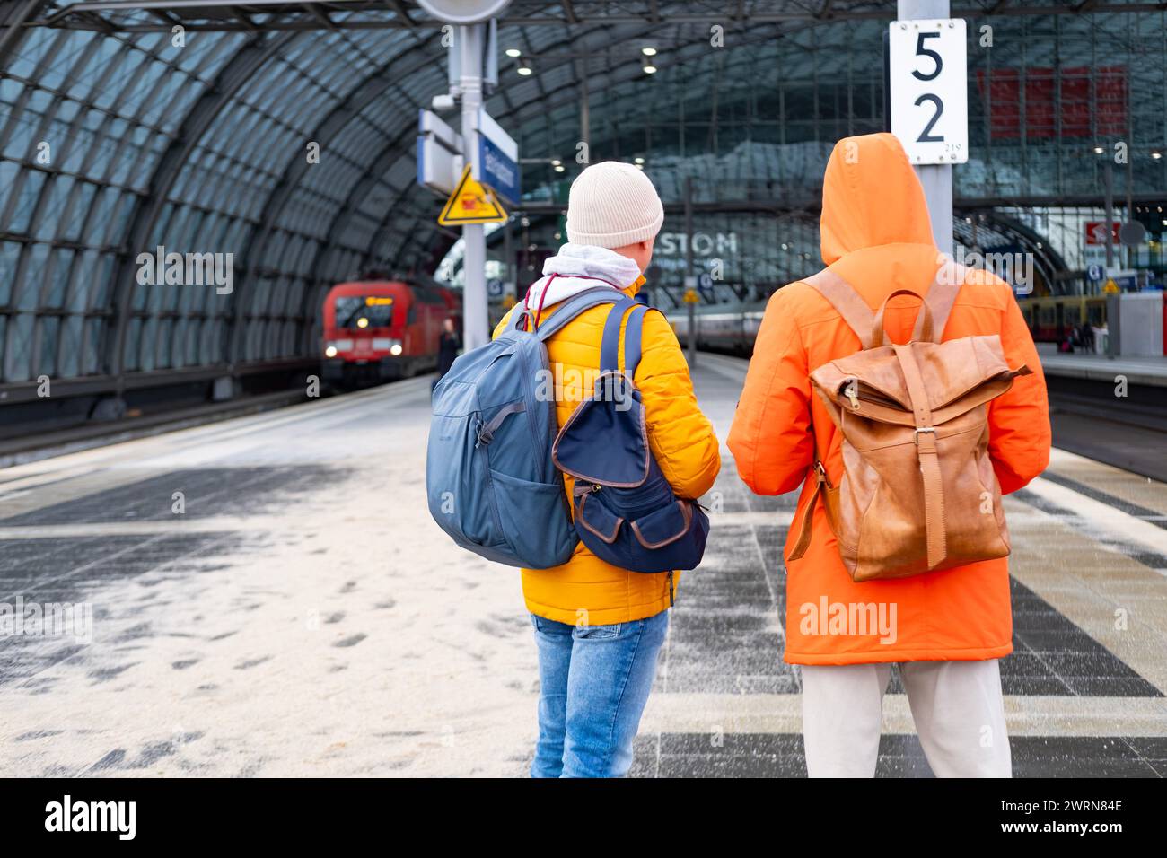 Zwei Männer in orangefarbenen Jacken am Bahnhof, Passagiere mit Rucksäcken warten auf den Zug, Berlin Hauptbahnhof, Concept Boarding Reisende im Auto, Hektik und Hektik Stockfoto
