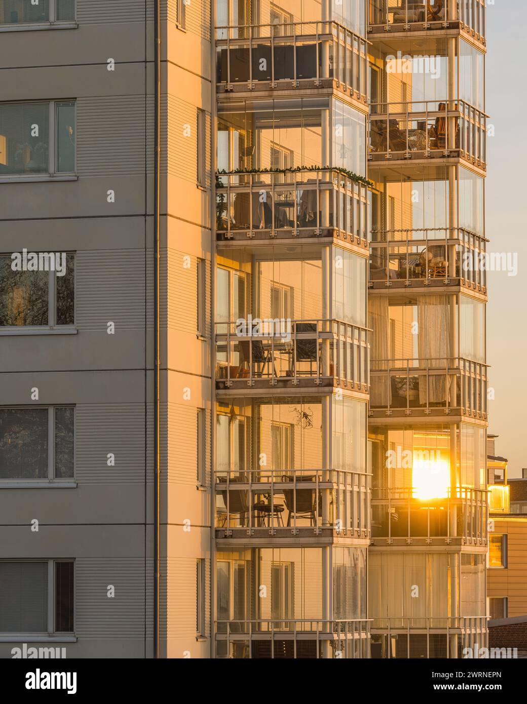 Ein hohes Wohngebäude in Göteborg, Schweden, mit zahlreichen Balkonen. Das Gebäude wird von den warmen Farbtönen des Sonnenaufgangs beleuchtet, wodurch ein Stockfoto