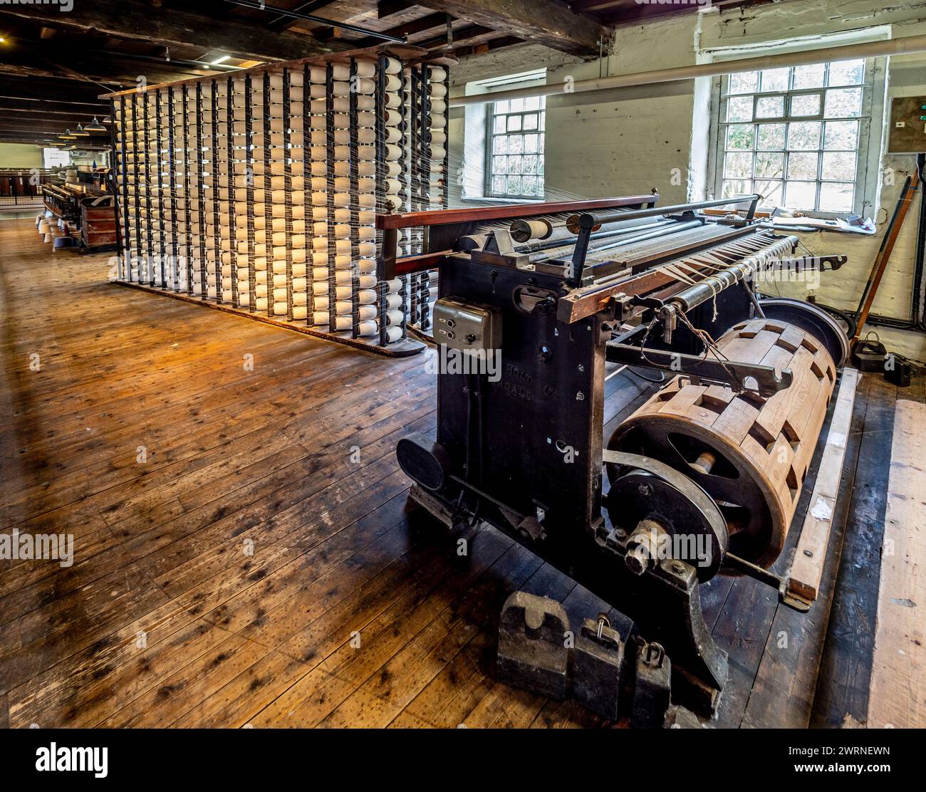 Wölbmaschine, die beim Weben von Baumwolle verwendet wird, mit Spulengestell dahinter. Quarry Bank Mill, Styal, Cheshire, Großbritannien Stockfoto
