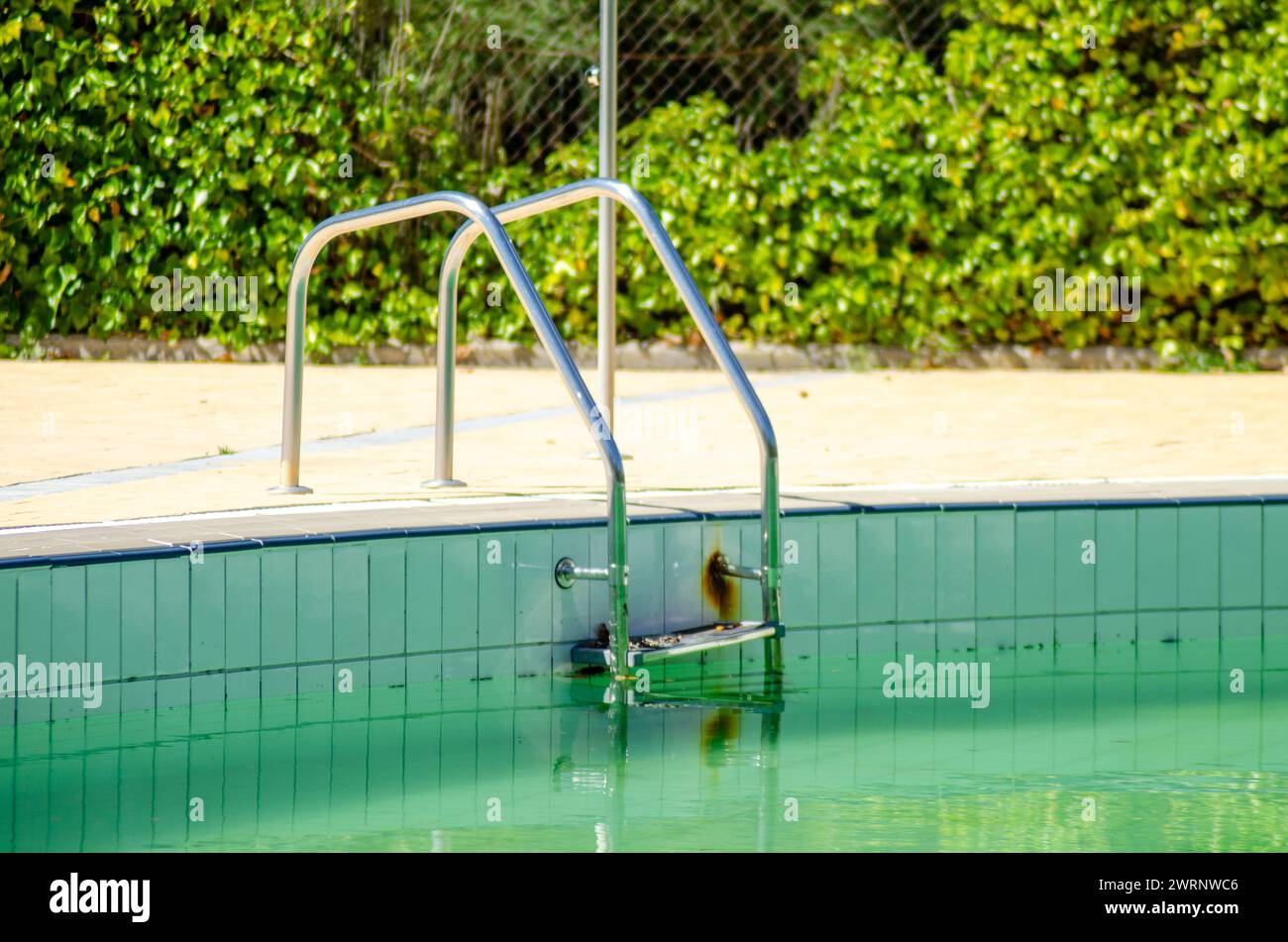 Metallleitern in einem Schwimmbad mit schmutzigem Wasser Stockfoto