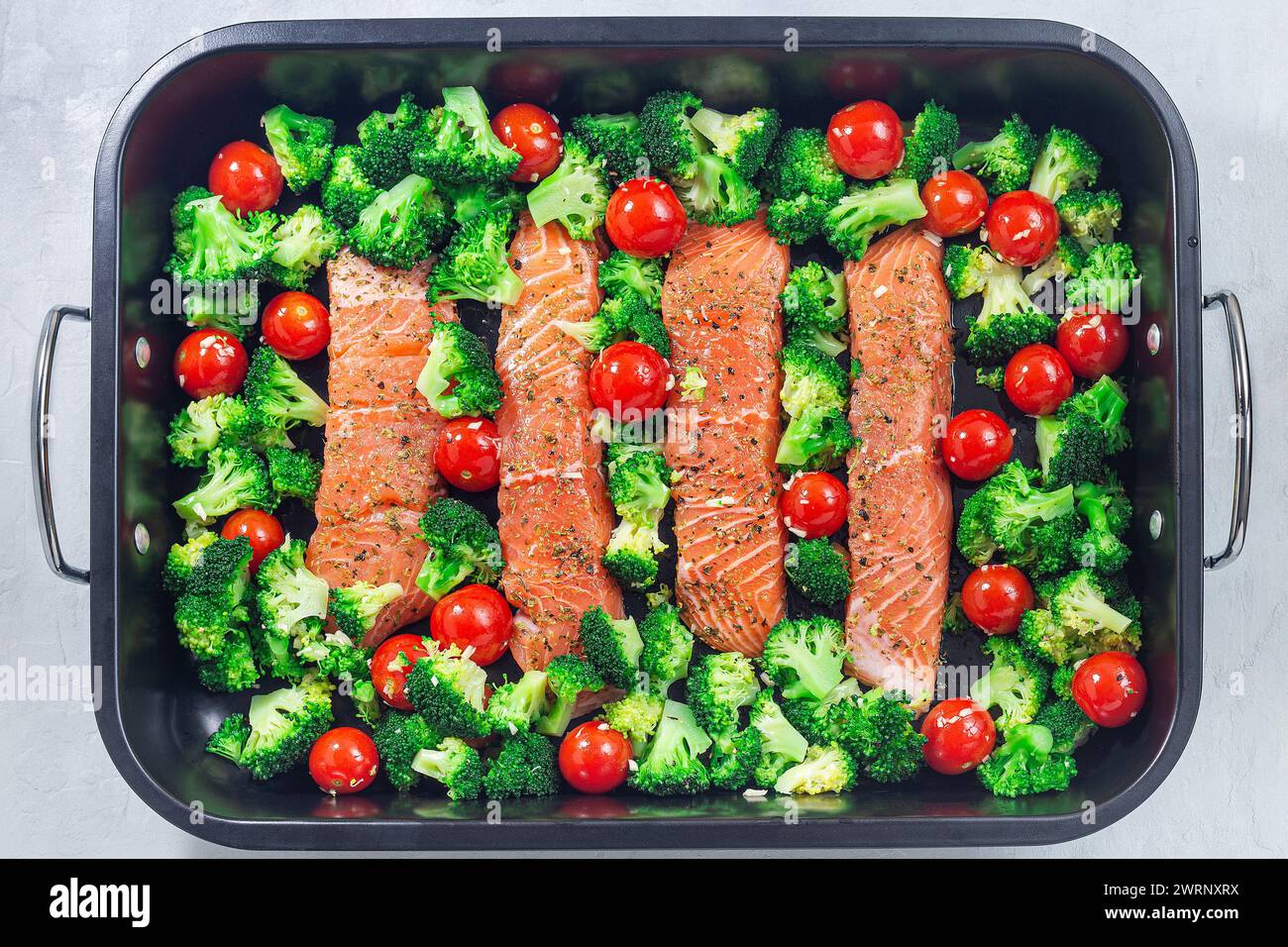 Rohes Lachsfilet mit Brokkoli und Tomaten auf einem Bratblech, bereit zum Backen, horizontal, Draufsicht Stockfoto