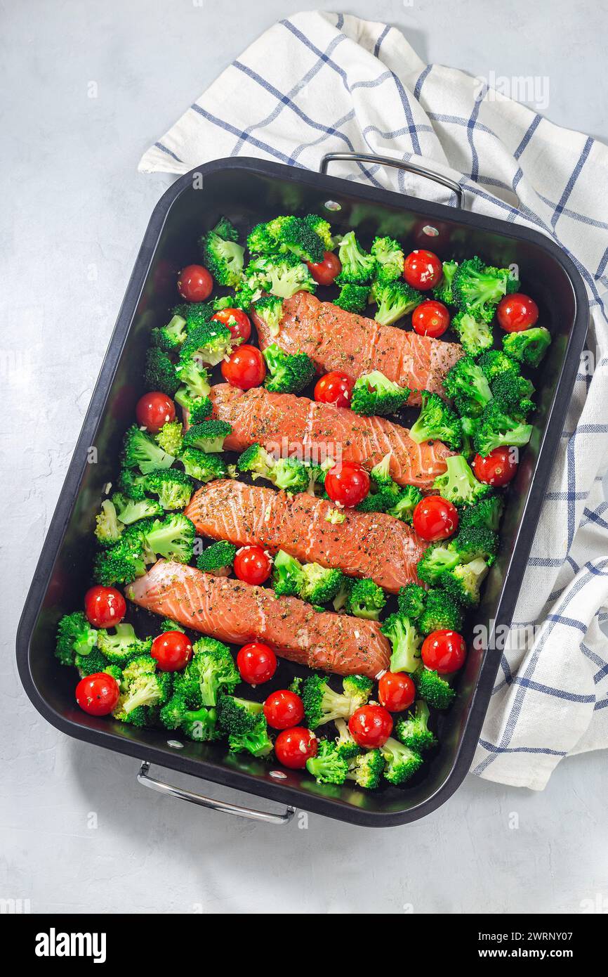 Rohes Lachsfilet mit Brokkoli und Tomaten auf einem Bratblech, fertig zum Backen, vertikal, Draufsicht Stockfoto