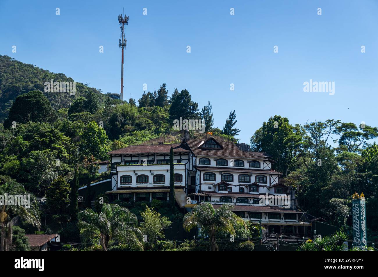 Blick auf das Gallardin Palace Hotel auf einem Hügel, umgeben von dichtem Waldgrün im Viertel Quitandinha unter sonnigem, klarem blauem Himmel. Stockfoto