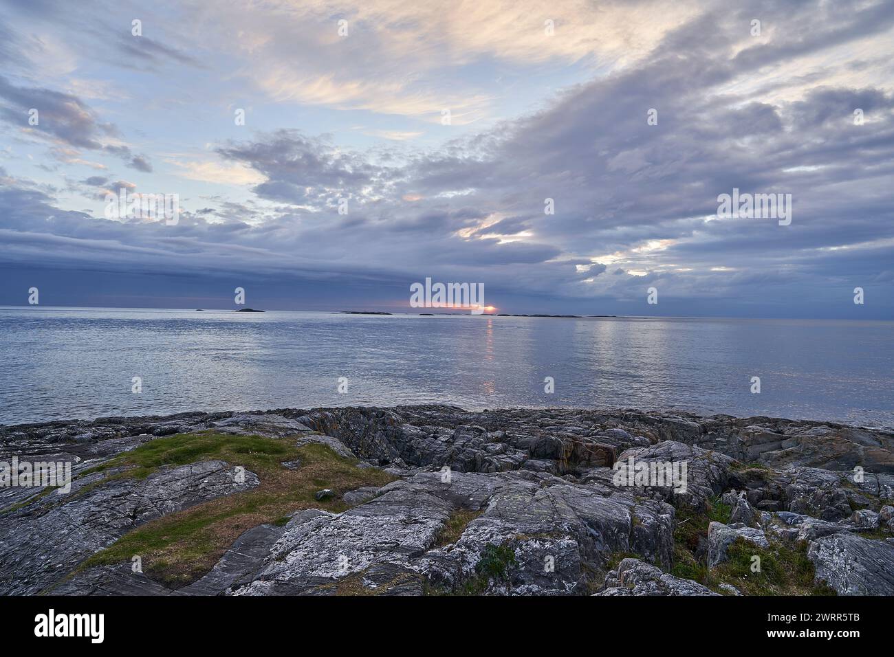 Dramatischer Sonnenuntergang über dem Nordatlantik an der zerklüfteten Küste Norwegens, mit einer orange leuchtenden Sonne und dunklen Wolken. Stockfoto