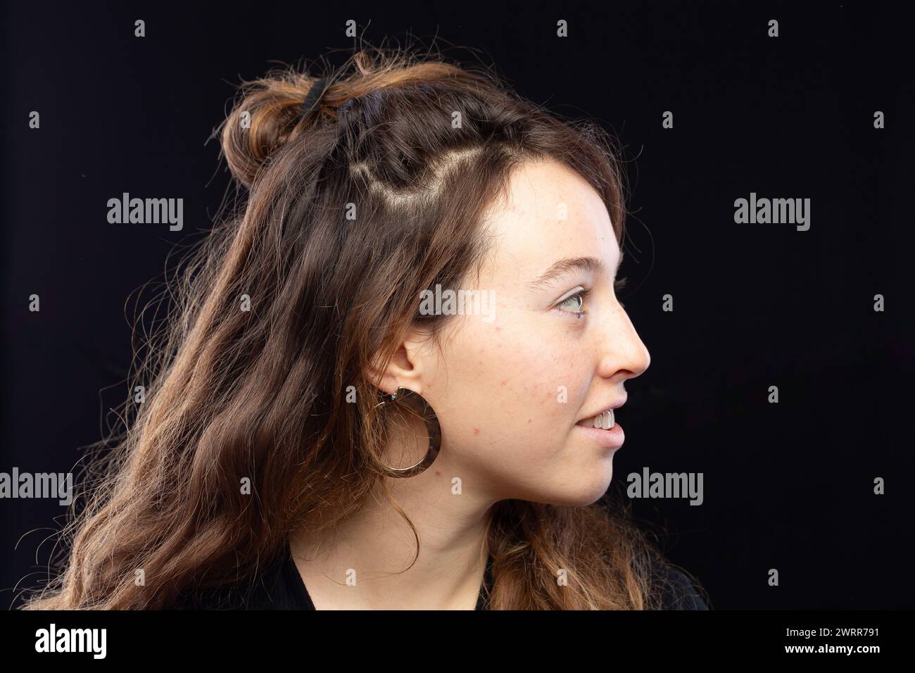 Profil einer jungen Frau, die ihre stilvollen Hochsteckungs- und Creolen-Ohrringe zeigt Stockfoto