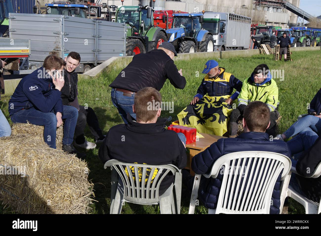Gent, Belgien. März 2024. Die Bauern haben sich mit Gartenstühlen, Strohballen und einem Tisch bei einem Bauernprotest, der am Donnerstag, den 14. März 2024 die Einfahrt von LKWs zum Hafen von Gent blockierte, bequem gemacht. Zwei unabhängige Junglandwirte-Verbände protestieren weiterhin gegen die strengen Stickstoffvorschriften für Landwirte. Durch die Sperrung der Häfen wollen die Landwirte darauf hinweisen, dass es vor allem die Industrie ist, die Stickstoff ausstößt, und nicht die Landwirtschaft. BELGA FOTO NICOLAS MAETERLINCK Credit: Belga News Agency/Alamy Live News Stockfoto