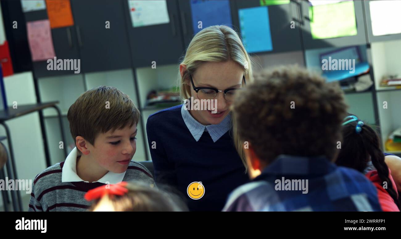 Bild von Emoji-Ikonen über lächelnde weiße Lehrerin mit verschiedenen Schülern, die sprechen Stockfoto