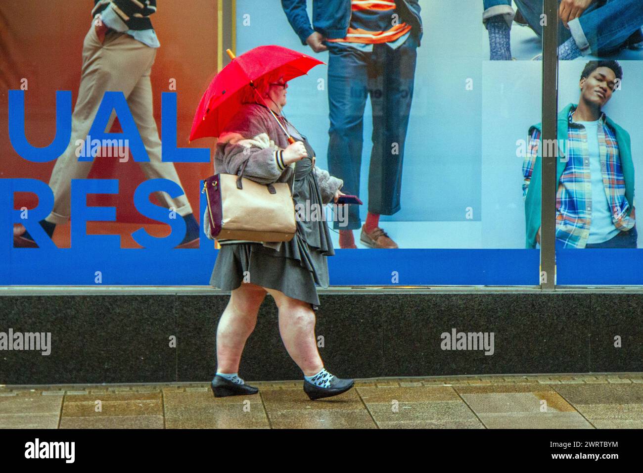 Frau mit roten Regenschirmen an regnerischen Tagen in Preston, Lancashire. Wetter in Großbritannien. März 2024. Regnerischer Start in den Tag für Shopper im Stadtzentrum. Wind mit heftigeren Regenfällen. Credit; MediaWorldImages/AlamyLiveNews Stockfoto