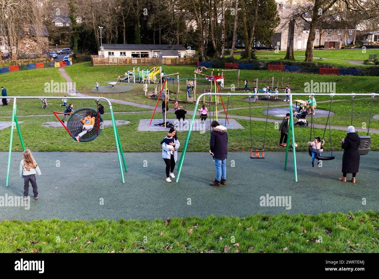 Eltern und Kinder spielen auf Schaukeln auf dem Spielplatz Priory Park in Bodmin Town in Cornwall in Großbritannien. Stockfoto