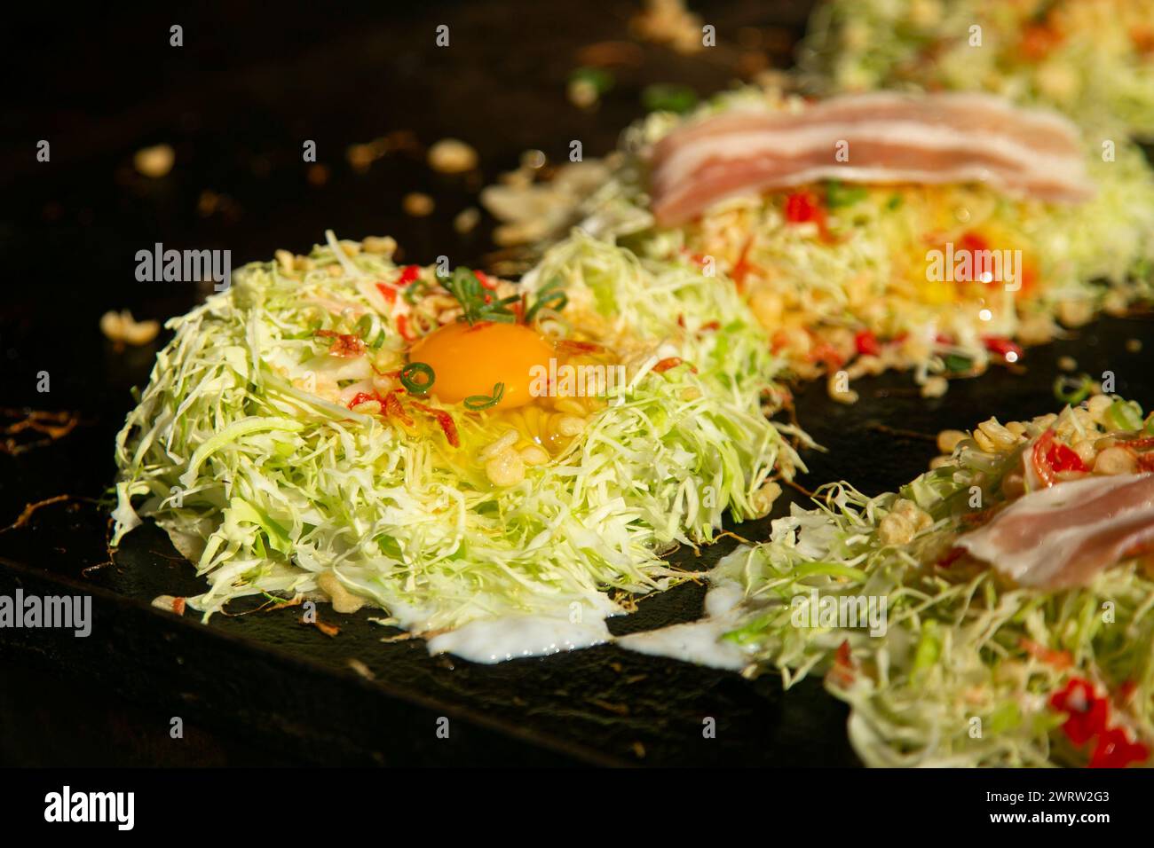 Okonomiyaki ist ein pikanter japanischer Kohl-Pfannkuchen, der „nach Belieben gegrillt“ wird, mit Proteinen und leckeren Gewürzen und Toppings. Stockfoto