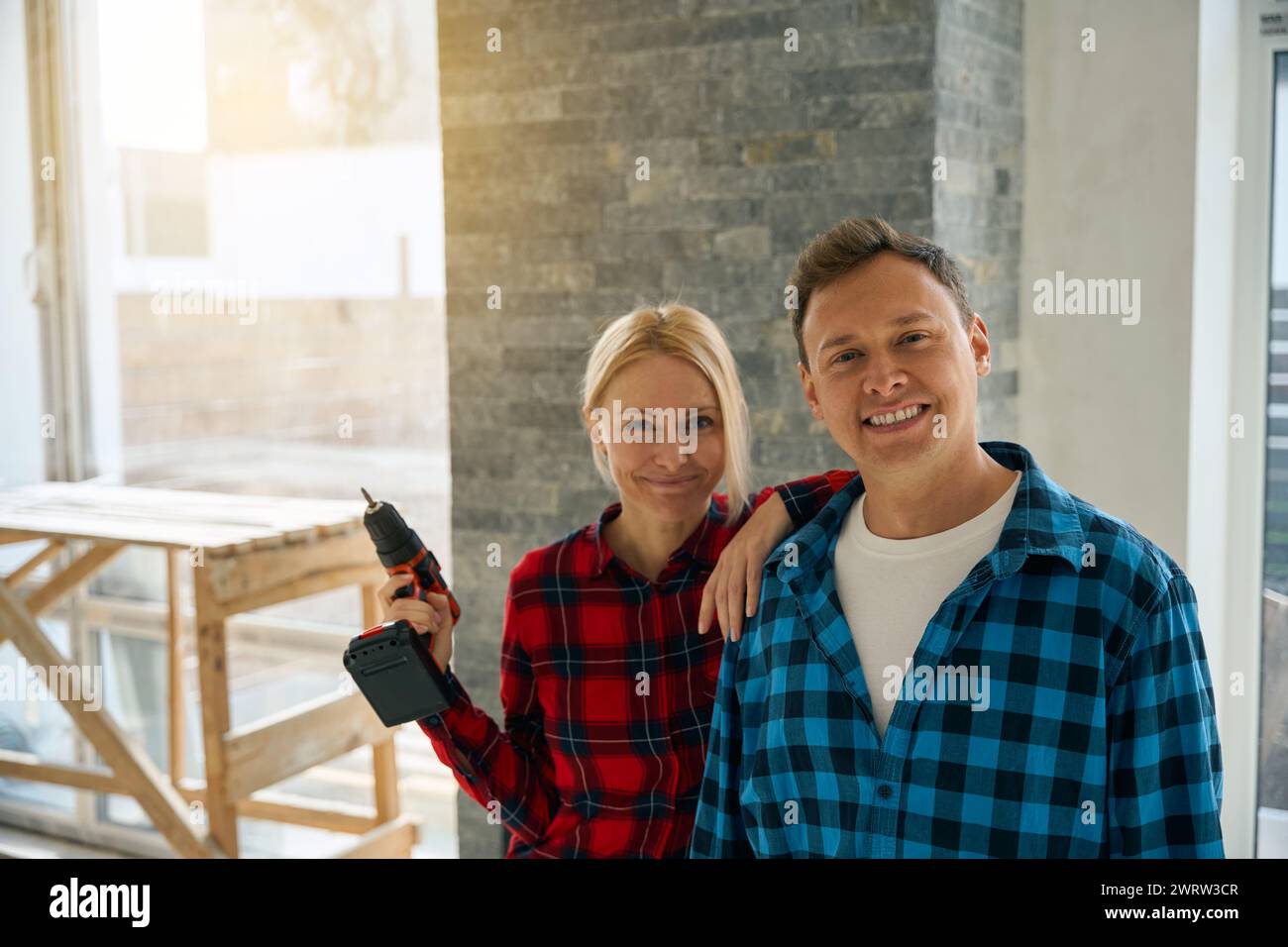 Das Bild von einem lächelnden Mann, der neben einer freudigen Dame steht, die einen elektrischen Schraubenzieher in der erhobenen Hand hält Stockfoto