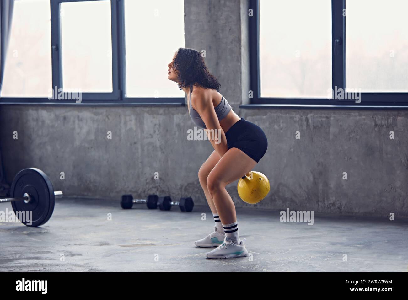 Seitenansicht einer konzentrierten jungen Frau, eines Sportlers in Sportbekleidung, der Sport treibt, Lifte, schwingt die Kettlebell über dem Kopf in Bewegung. Stockfoto