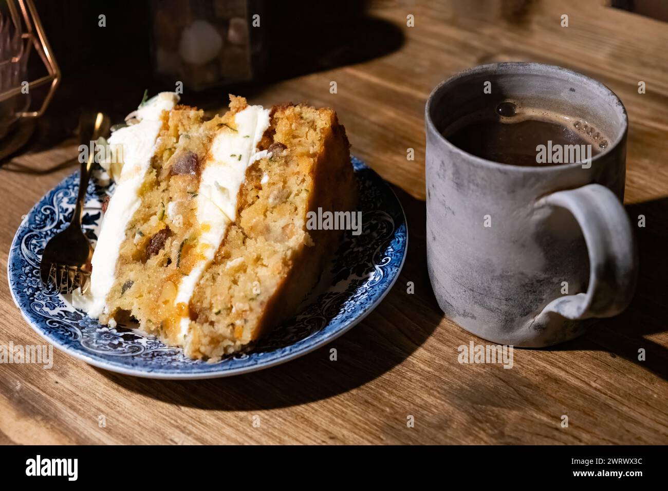 Ein frisch gebackenes Stück veganer Karotten- und Zucchini-Kuchen. Der Kuchen wird auf einem Café-Tisch mit einer frischen Tasse schwarzen Kaffee serviert Stockfoto