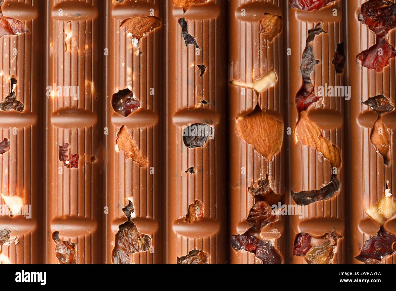 Schokoladenhintergrund. Milchschokolade mit Mandeln, Rosinen, trockenen Beeren aus nächster Nähe als Hintergrund. Stockfoto