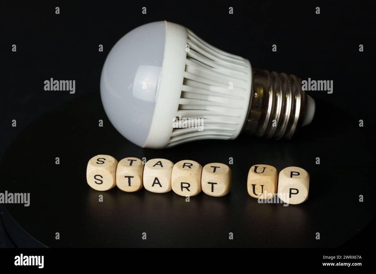 Eine Glühbirne liegt neben hölzernen Buchstabenblöcken, die das START-UP beschreiben und den Beginn eines neuen Unternehmens symbolisieren. Stockfoto
