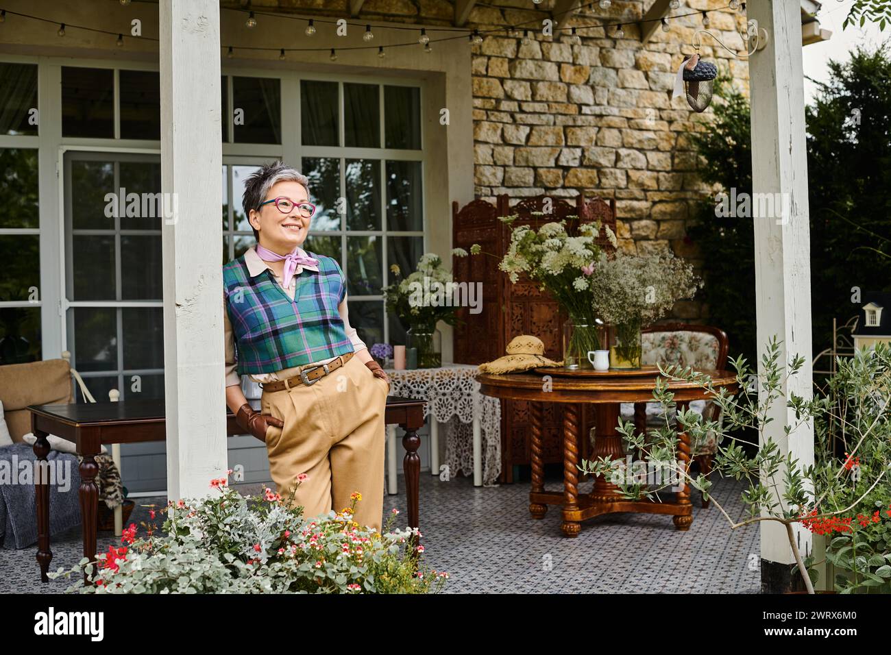 Aristokratische, fröhliche Frau mit Brille, die neben ihrem Haus in England posiert und wegblickt Stockfoto