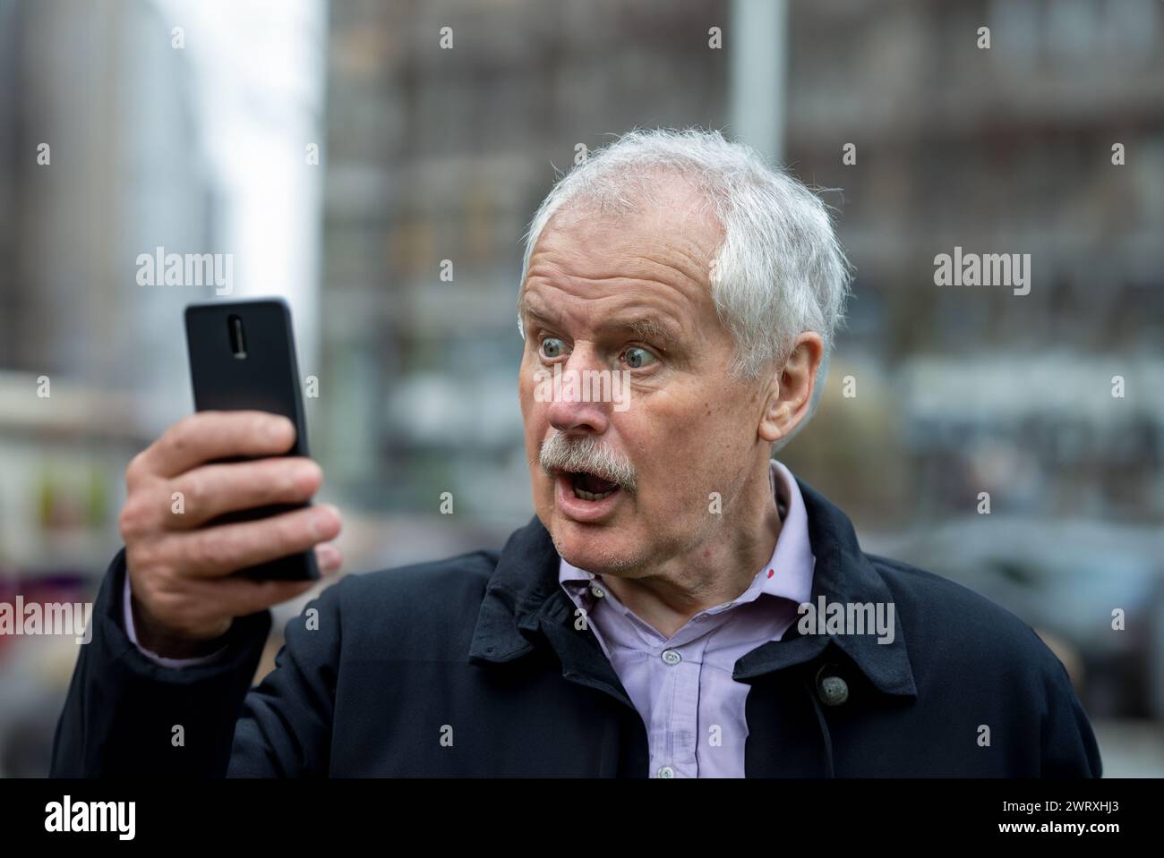 Senior-Mann, der sich schockiert an seinem Handy. Stockfoto