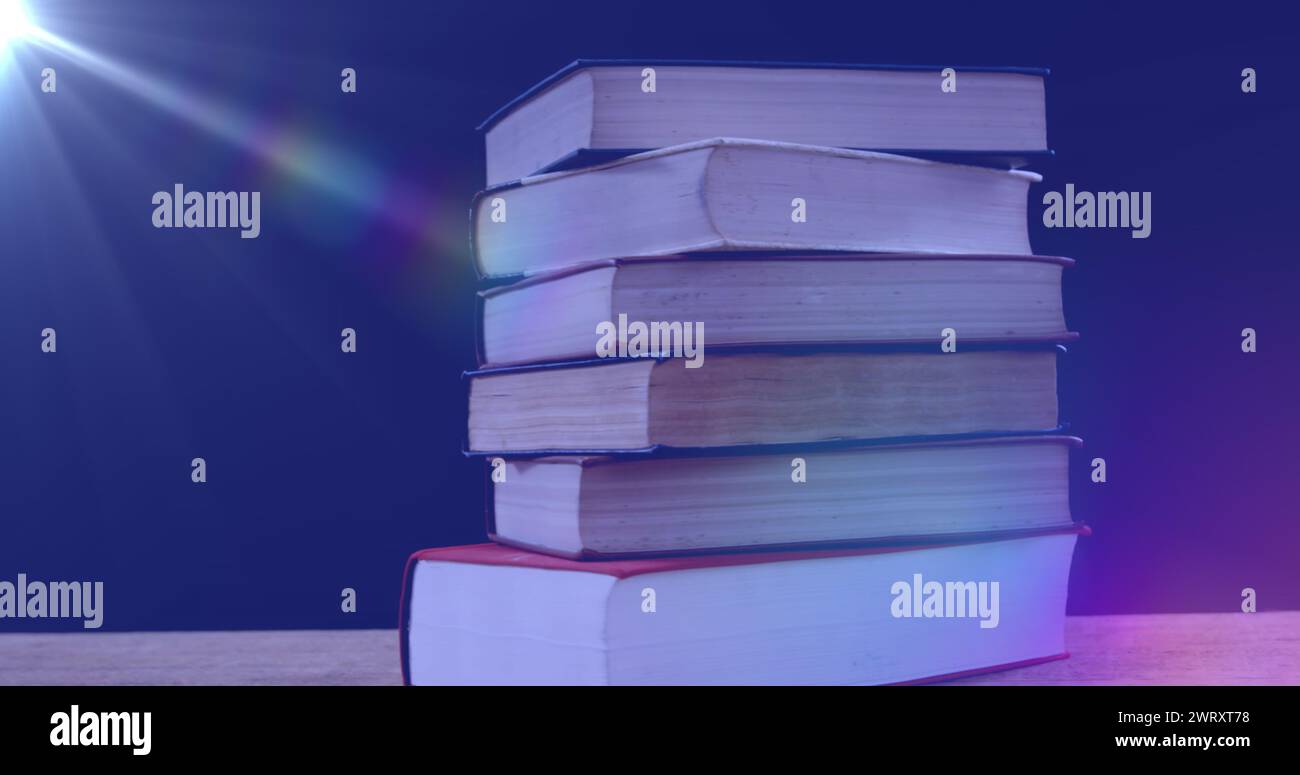 Bild von leuchtendem Licht über einem Stapel Bücher auf blauem Hintergrund Stockfoto