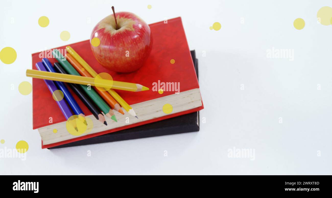 Bild von gelben Flecken über Apfel und Farbstiften auf einem Stapel Bücher Stockfoto