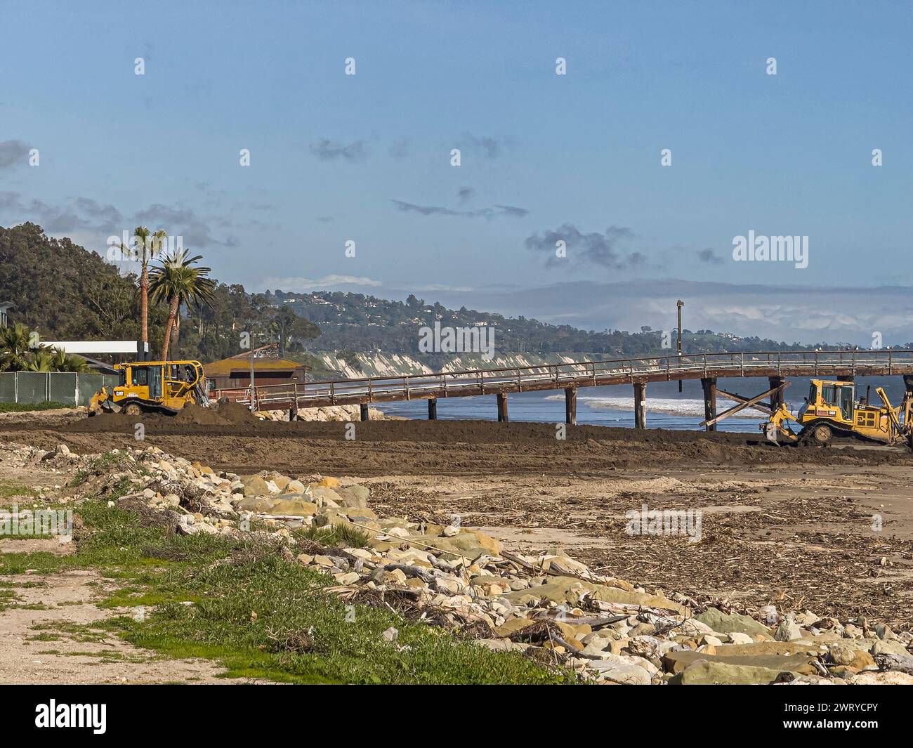 Santa Barbara, Kalifornien, USA - 11. März 2024:: Bulldozer schieben dunkelbraunen Schmutz über Sandstrand in den Pazifik am Fuße des Goleta Piers unter blu Stockfoto