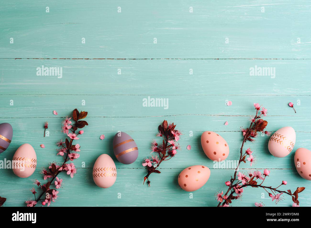 Osterflachlage mit bemalten Eiern, Kirschblüten und Blütenblättern auf türkisblauem Hintergrund. Draufsicht, Kopierraum. Stockfoto