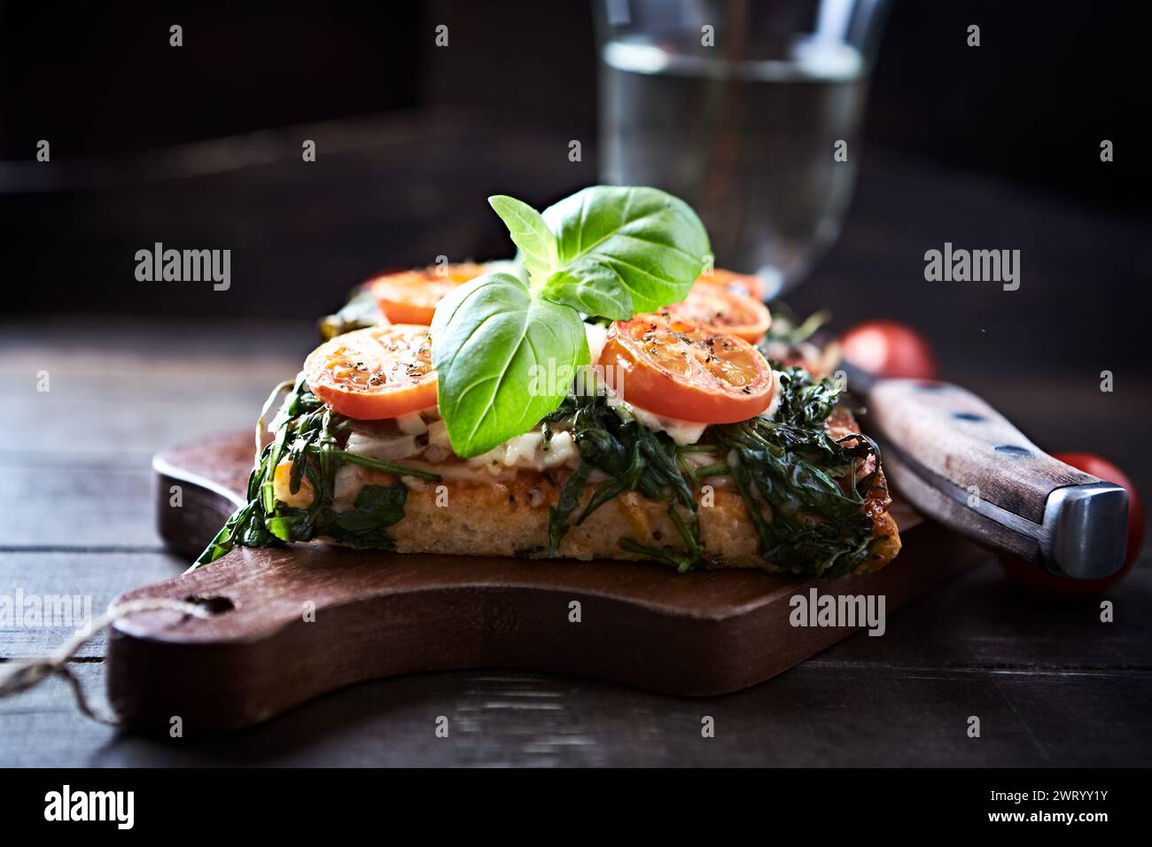 Offenes, geröstetes Käse-Sandwich mit Kirschtomaten, Spinat und frischem Basilikum. Brauner Holzhintergrund. Stockfoto