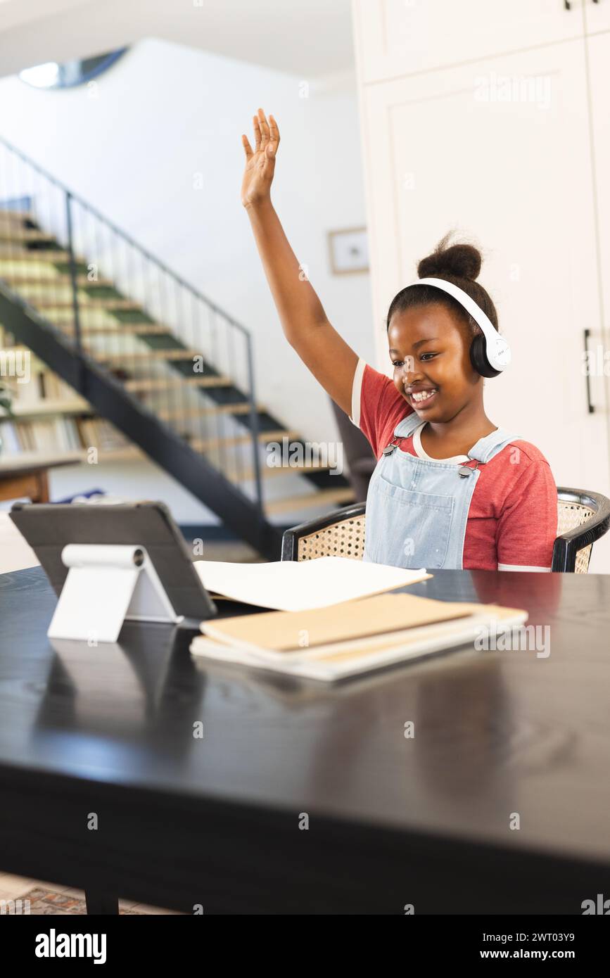 Ein junges afroamerikanisches Mädchen hebt ihre Hand während eines virtuellen Kurses zu Hause Stockfoto