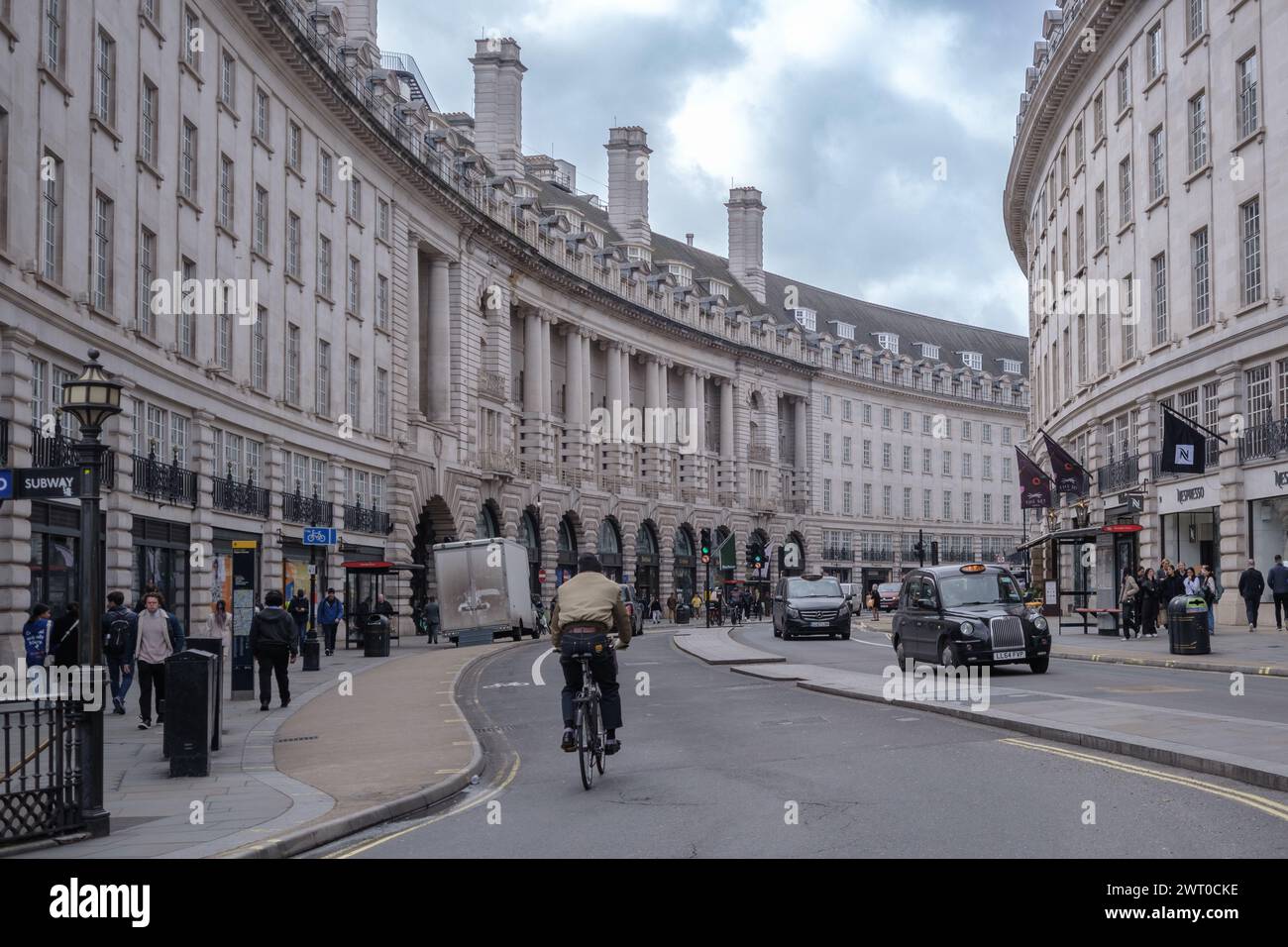 Radfahrer fahren auf der Regent Street London, gesäumt von historischen Gebäuden, Geschäften und Fußgängern unter bewölktem Himmel. Stockfoto