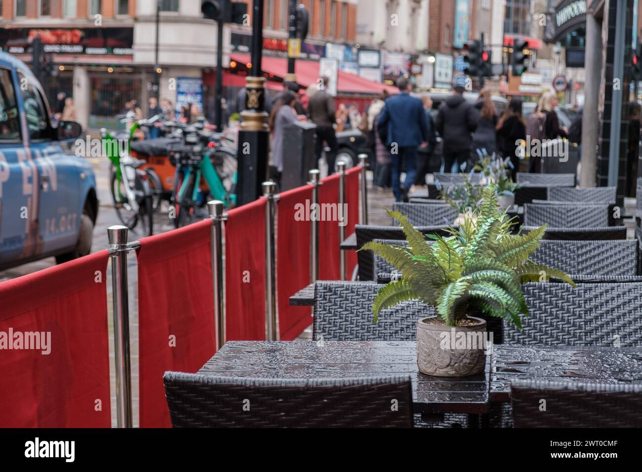Café auf dem Bürgersteig mit Korbstühlen und Tischen mit Topfpflanzen, nass vor Regen. Geschäftiges Stadtleben. Zentrum Von London, England. Stockfoto