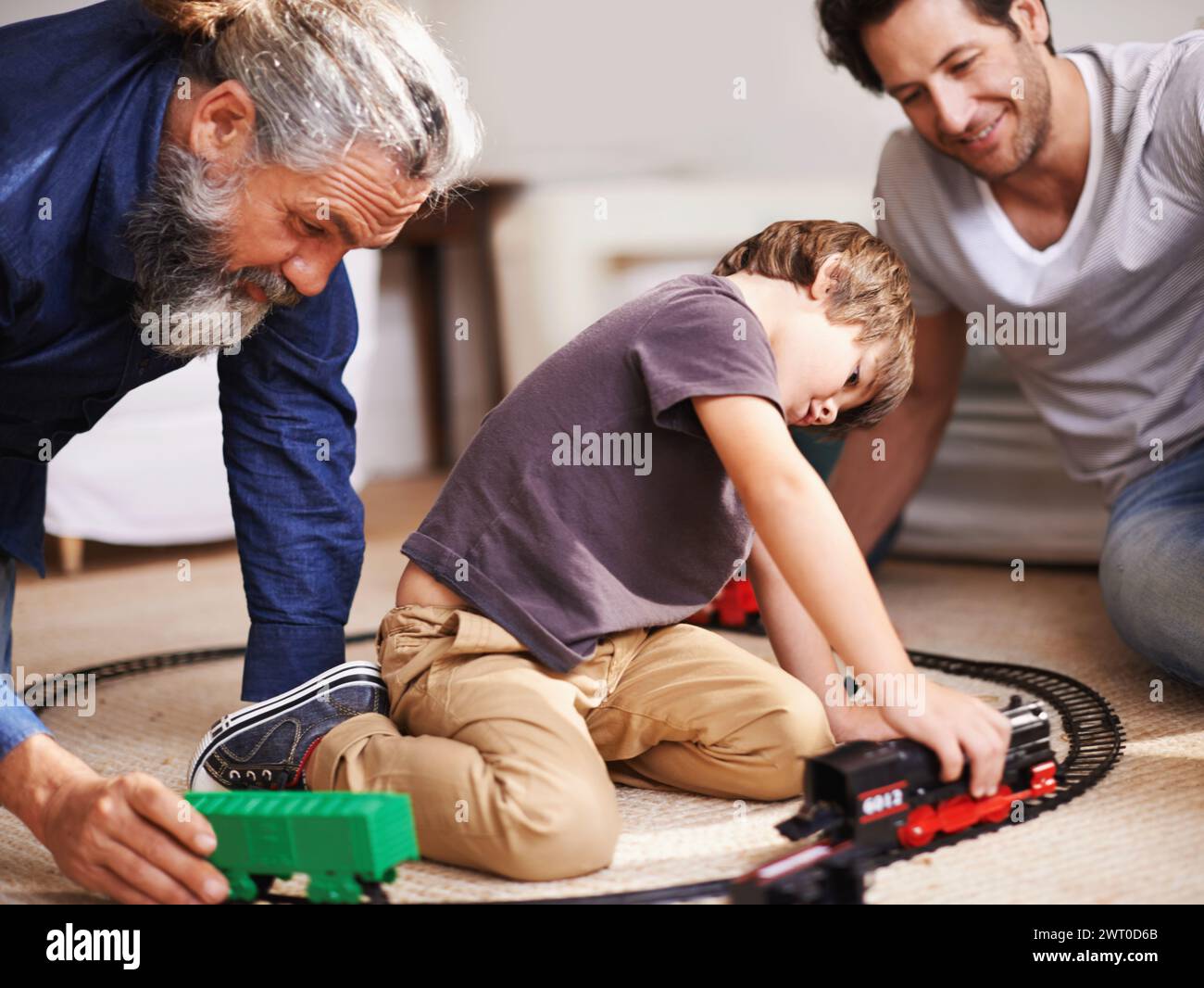 Männer, Jungen und spielen mit Zugspielzeug, zusammen für die Familie und Spaß auf der Plastikbahn zu Hause. Großvater, Vater und Kind mit Stockfoto
