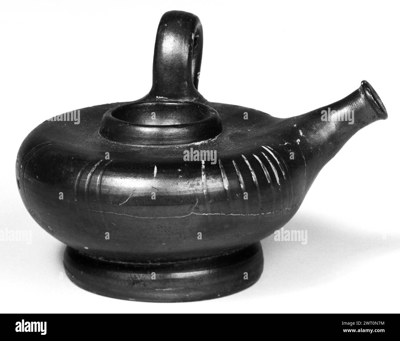 Campanian Black Guttus mit Sieb Top. Unbekannt 323–31 v. Chr. der kreisförmige Griff ist senkrecht zu einem nach oben zeigenden Mund in Form eines zylindrischen Tubus. In der Mitte der oberen, leicht konkaven Oberfläche des Gefäßes befindet sich eine kreisförmige Kante, innerhalb der sechs Perforationen angeordnet sind, wobei fünf in der Mitte eine Perforation umgibt. Die Oberfläche ist mit schwarzem Glanz bedeckt, bewahren Sie die Unterseite des unteren Fußes auf. Es gibt Gruppen vertikaler Schnittlinien um das Äußere, in Gruppen von zwei bis acht. Es gibt viele Spuren von cremefarbener Farbe. Stockfoto