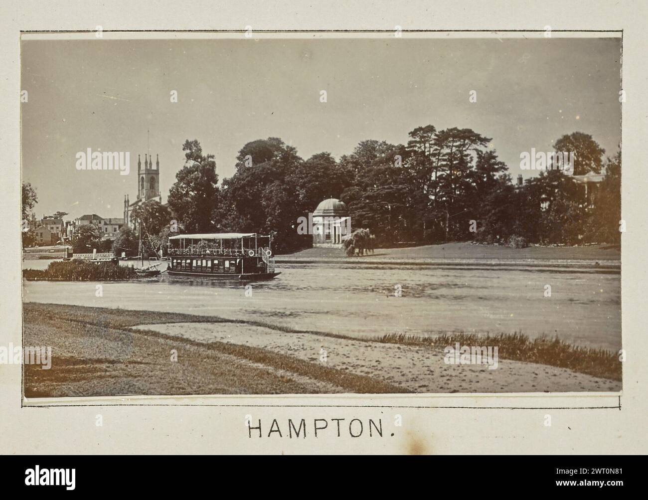 Hampton. Henry W. Taunt, Fotograf (Britisch, 1842 - 1922) 1897 eines von drei Fotos mit Tippeingabe, die eine gedruckte Karte von Kingston und der Umgebung, einschließlich Hampton Court Park und Bushy Park, entlang der Themse, illustrieren. Das Foto zeigt einen Blick auf den Fluss bei Hampton, mit dem Turm von St. Marienkirche sichtbar über den Bäumen in der Ferne. Eine Fähre, die einen Lastkahn zieht, fährt den Fluss entlang, vorbei am Garrick's Temple nach Shakespeare, einem kleinen, gewölbten Pavillon mit einem Portikus auf der anderen Seite des Flusses. (Recto, Mount) unten in der Mitte, unter dem Bild, in schwarzer Tinte gedruckt: 'HAMPTON'. Stockfoto Hampton. Henry W. Taunt, Fotograf (Britisch, 1842 - 1922) 1897 eines von drei Fotos mit Tippeingabe, die eine gedruckte Karte von Kingston und der Umgebung, einschließlich Hampton Court Park und Bushy Park, entlang der Themse, illustrieren. Das Foto zeigt einen Blick auf den Fluss bei Hampton, mit dem Turm von St. Marienkirche sichtbar über den Bäumen in der Ferne. Eine Fähre, die einen Lastkahn zieht, fährt den Fluss entlang, vorbei am Garrick's Temple nach Shakespeare, einem kleinen, gewölbten Pavillon mit einem Portikus auf der anderen Seite des Flusses. (Recto, Mount) unten in der Mitte, unter dem Bild, in schwarzer Tinte gedruckt: 'HAMPTON'. Stockfoto