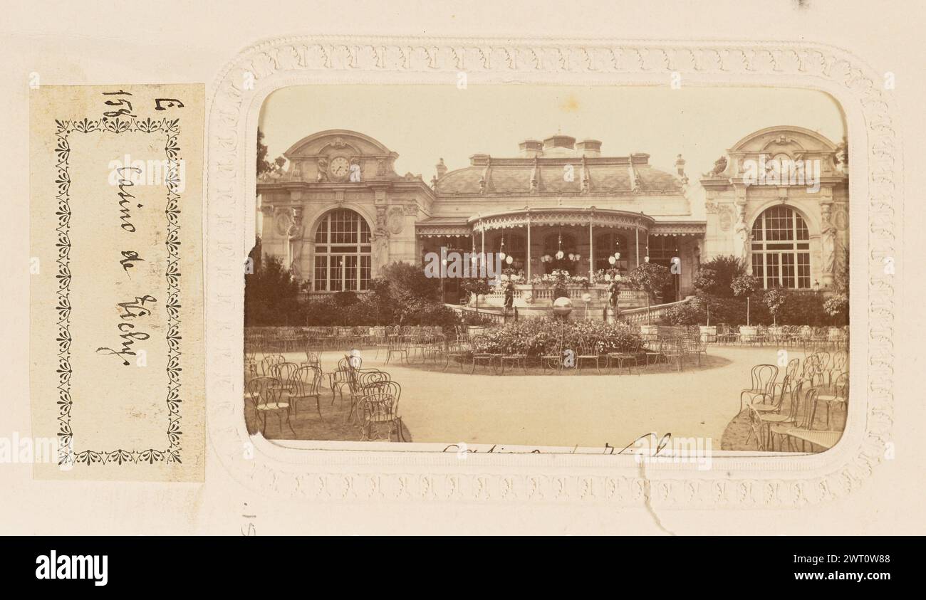 Casino de Vichy. Unbekannt, Fotograf nach 1865 Blick auf das Casino de Vichy ein großes Gebäude mit einer kreisförmigen Fahrt davor. Mehrere Tische und Stühle sind auf dem Rasen rund um die Straße aufgestellt. Das Gebäude hat eine kreisförmige Struktur, die einem Pavillon ähnelt und sich von der Mitte der Fassade erstreckt. (Recto, Mount) untere Mitte, schwarze Tinte: 'Casino de Vichy'; (Verso, Mount) untere Mitte, schwarze Tinte: 'Casino Facade sur le Parc (Vichy)'; (Recto, Albumseite) untere Mitte, darunter Bild, schwarze Tinte auf weißem Papieretikett: 'E/158 [space] Casino de Vichy'; Stockfoto