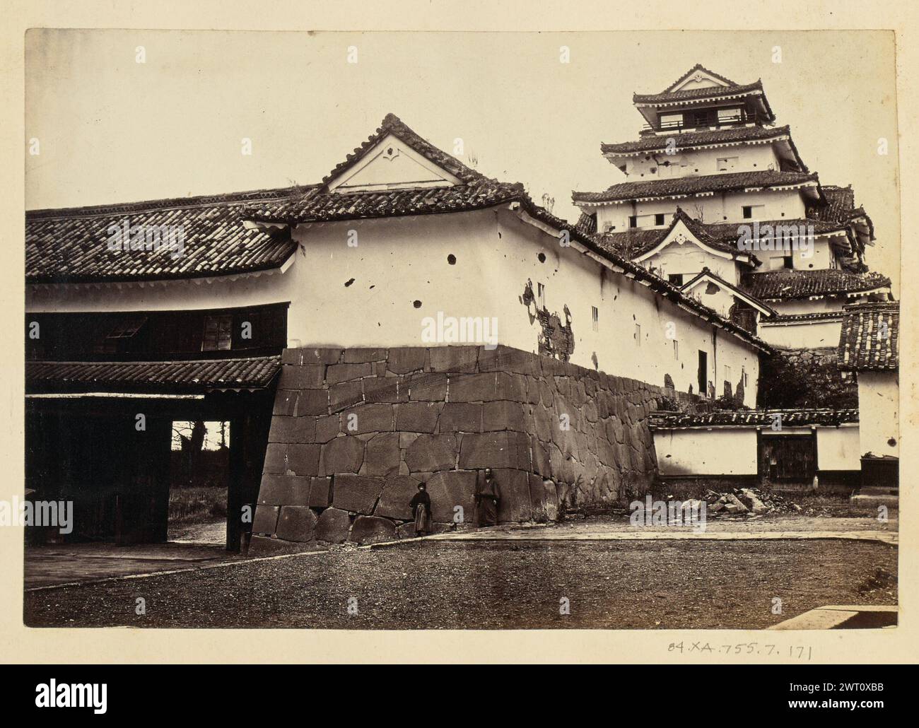 Schloss Tsuruga. Unbekannt, Fotograf vor 1873 Blick auf den ursprünglichen Tenshu von Tsuruga-Jo direkt außerhalb der umliegenden Mauer. Zwei Männer stehen gegen die Wand, die der Kamera zugewandt ist. Stockfoto