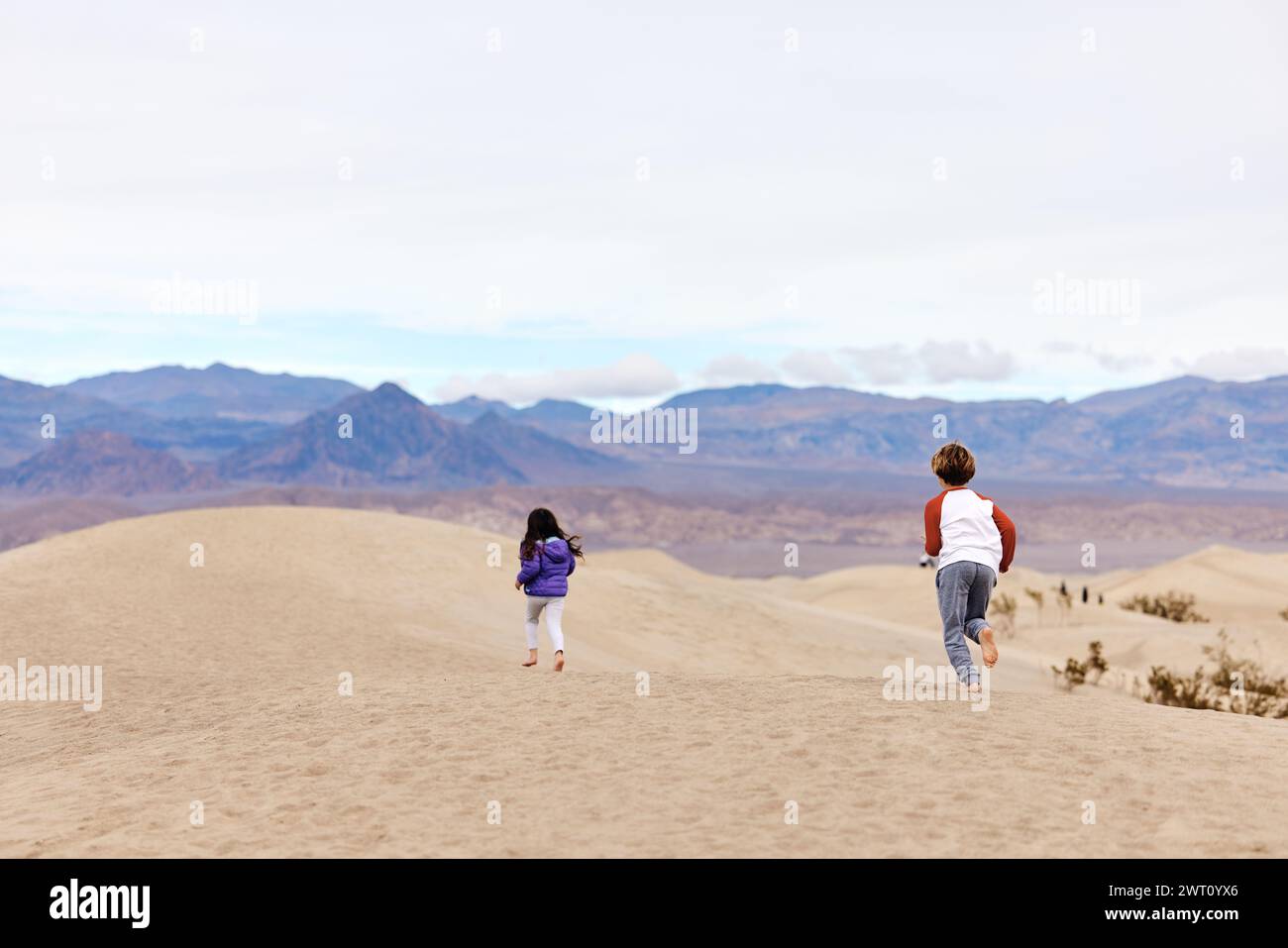 Rückansicht unbeschwerter Geschwister, die auf Sanddünen im Death Valley laufen Stockfoto