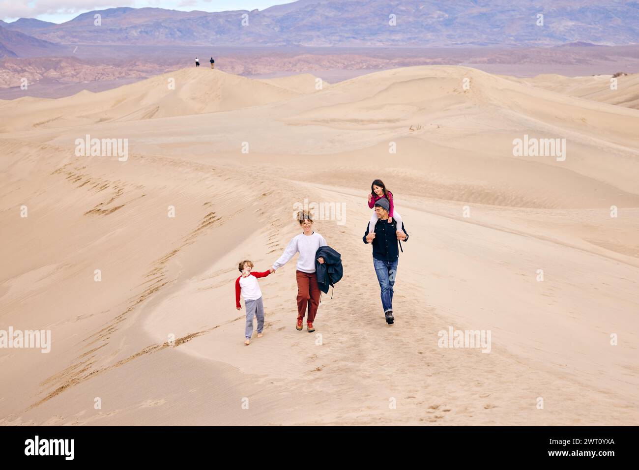 Vater und Mutter mit Kindern, die im Urlaub über Sanddünen laufen Stockfoto