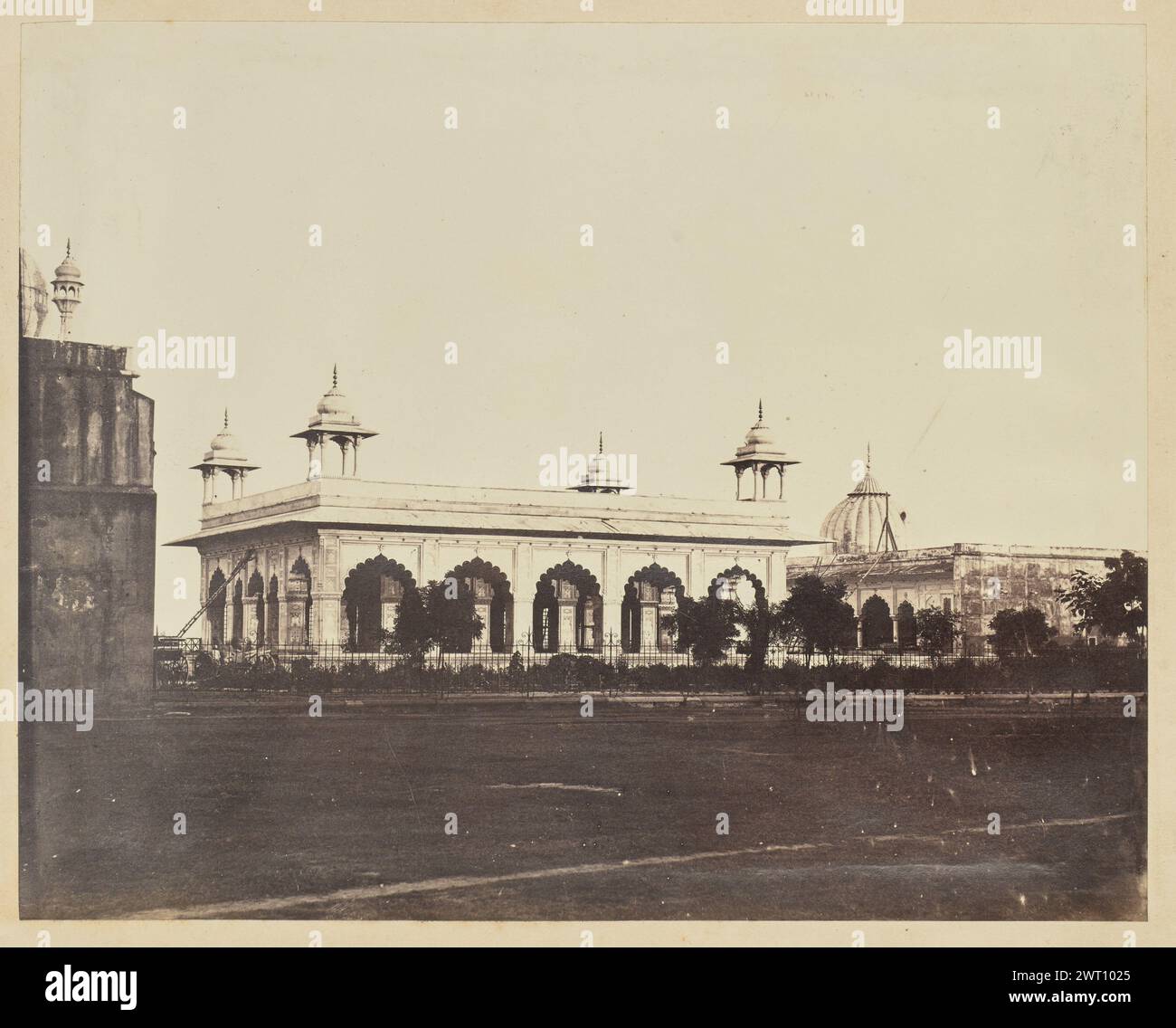 Die Diwan-i-Khas im Roten Fort von Delhi. Unbekannt, Fotograf der 1850er–1890er Jahre Ansicht des Diwan-i-Khas im Roten Fort von Delhi. Das Gebäude verfügt über gewölbte Bögen, detaillierte Intarsien und vier Chhatri oder Kuppelpavillons an den Ecken des Daches. Ein Mann ruht auf einer Leiter, die sich an der linken Seite des Gebäudes, möglicherweise zur Reinigung oder Reparatur, in der Nähe von zwei Pferdekutschen anlehnt. Ein schmiedeeiserner Zaun führt am Diwan-i-Khas vorbei und trennt ihn vom grasbewachsenen Rasen im Vordergrund. Die Kuppel des Khas Mahal ist hinter dem Pavillon auf der rechten Seite des Bildes sichtbar. Stockfoto Die Diwan-i-Khas im Roten Fort von Delhi. Unbekannt, Fotograf der 1850er–1890er Jahre Ansicht des Diwan-i-Khas im Roten Fort von Delhi. Das Gebäude verfügt über gewölbte Bögen, detaillierte Intarsien und vier Chhatri oder Kuppelpavillons an den Ecken des Daches. Ein Mann ruht auf einer Leiter, die sich an der linken Seite des Gebäudes, möglicherweise zur Reinigung oder Reparatur, in der Nähe von zwei Pferdekutschen anlehnt. Ein schmiedeeiserner Zaun führt am Diwan-i-Khas vorbei und trennt ihn vom grasbewachsenen Rasen im Vordergrund. Die Kuppel des Khas Mahal ist hinter dem Pavillon auf der rechten Seite des Bildes sichtbar. Stockfoto
