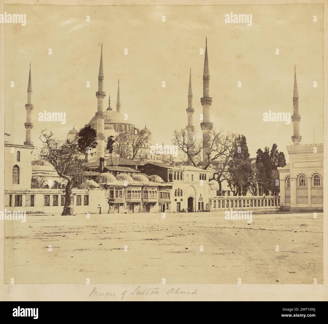 Moschee von Sultan Ahmed. Unbekannt, Fotograf der 1850er–1890er Jahre Blick auf die Sultan-Ahmed-Moschee, auch bekannt als Blaue Moschee, von einem Platz außerhalb der Umrandung. Das zentrale Gebäude mit seinen zahlreichen Kuppeln und Minaretten ist hinter der Mauer sichtbar, die ein Tor und eine kurze Reihe kleinerer Gebäude direkt neben dem Eingang aufweist. Zwei Figuren sitzen auf beiden Seiten des bogenförmigen Eingangs im Tor. Eine hölzerne Leiter lehnt sich an einen Baum, der direkt außerhalb der Mauer auf der linken Seite des Bildes wächst. (Recto, Halterung) links unten, handgeschrieben mit Bleistift: '8'; unten in der Mitte, handgeschrieben mit Bleistift: Stockfoto