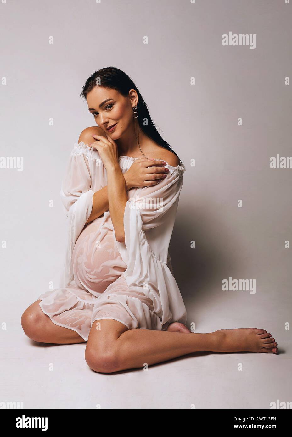 Schöne schwangere Frau mit nassem Haar und nassweißer Tunika Stockfoto