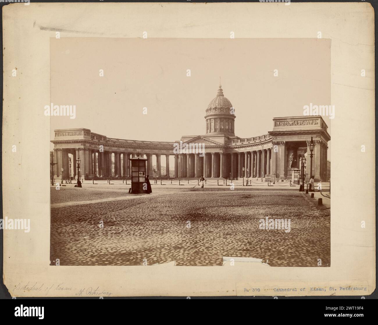 Kathedrale von Kasan, St. Petersburg. Unbekannt, Fotograf ca. 1875 Eine große Kathedrale mit einer gekrümmten Kolonnade. Das Gebäude in der Mitte der Kolonnade hat einen Giebel mit Reliefskulptur und ein kleines Kuppeldach. Es gibt eine kleine Kabine mit einem Mann in einem langen Mantel, der seitlich gelehnt ist. Ein Mann mit einer Schürze fegt den Innenhof. (Recto, Mount) unten links, schwarze Tinte: 'Kathedrale von Kasan [sic] - St. Petersburg". Stockfoto
