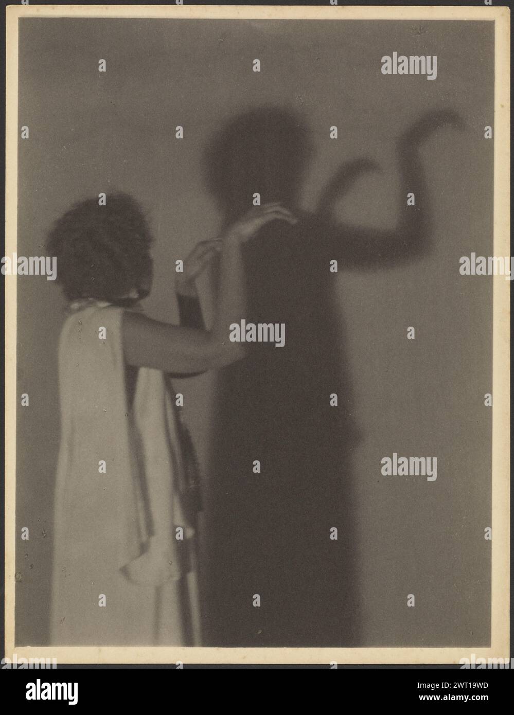 Frau macht Handschatten an der Wand. Doris Ulmann, Fotografin (Amerikanerin, 1882–1934) über 1929–1930 afroamerikanische Frau in einem weißen Kleid, mit dem Rücken von der Kamera abgewandt und Schatten an einer Wand erzeugt, mit beiden Armen nach oben. (Rückseitig, montiert) links unten, mit Bleistift: "28 [eingekreist]"; Stockfoto